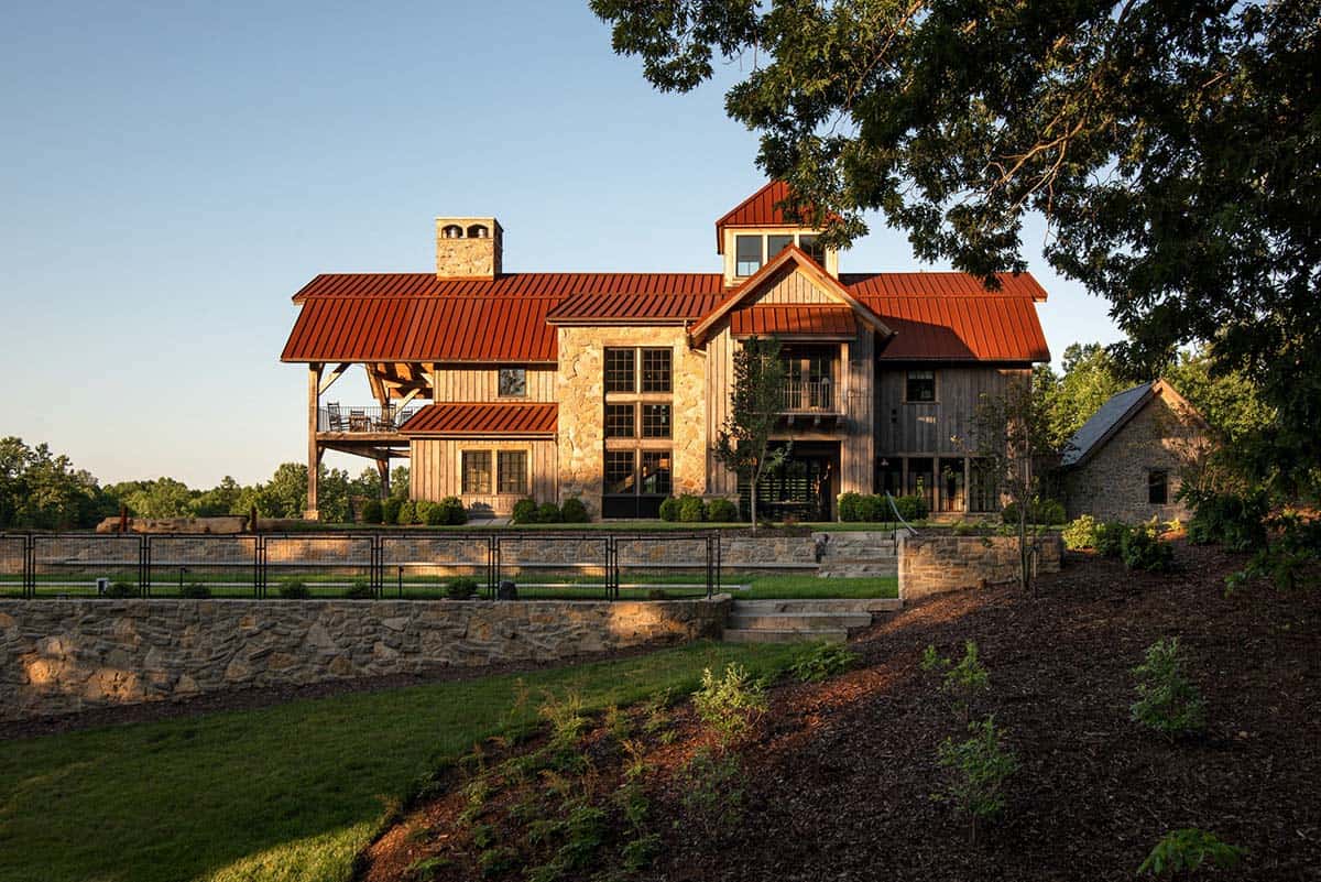 Rustic home with red roof above stone retaining walls and lawn