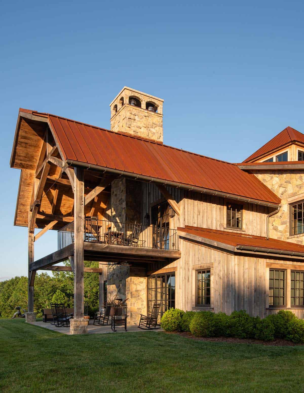 Two-story timber-frame porch with rocking chairs and stone chimney