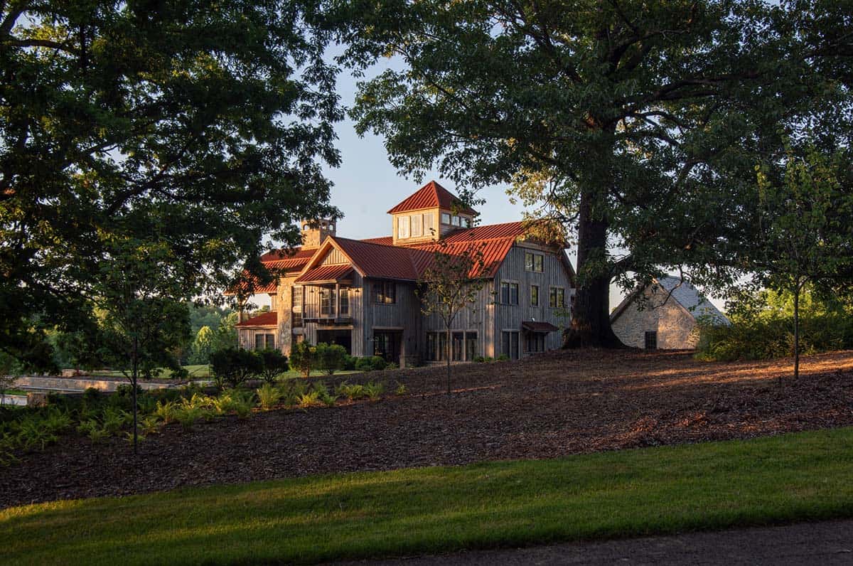 Rustic barn home with cupola framed by mature oak trees