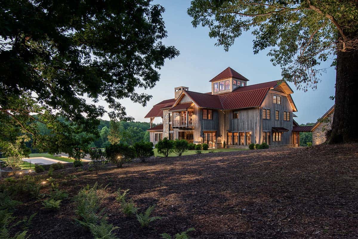 Barn-style home glowing at twilight beneath large oak trees