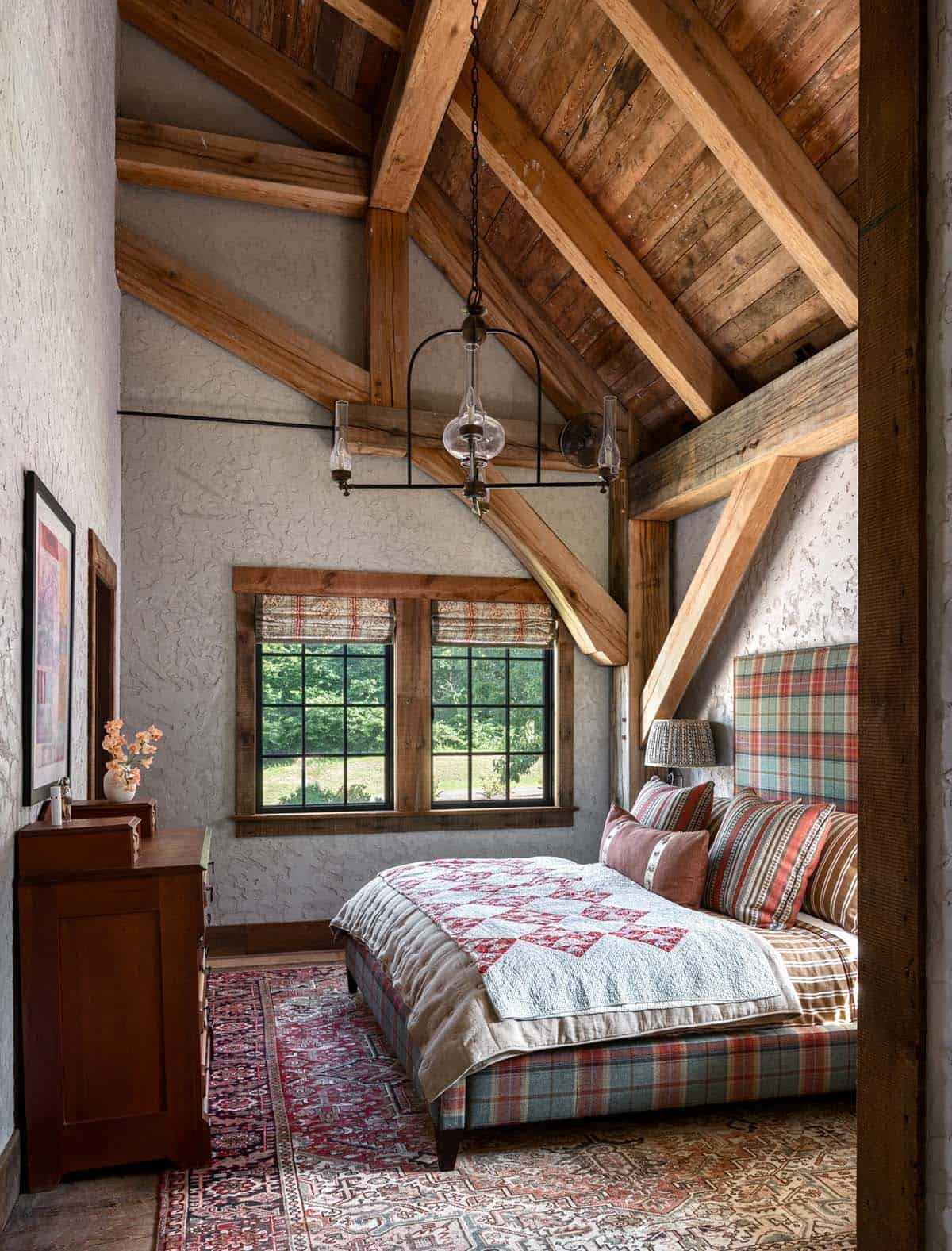 Bedroom with plaid upholstered bed, vintage quilt, and timber trusses