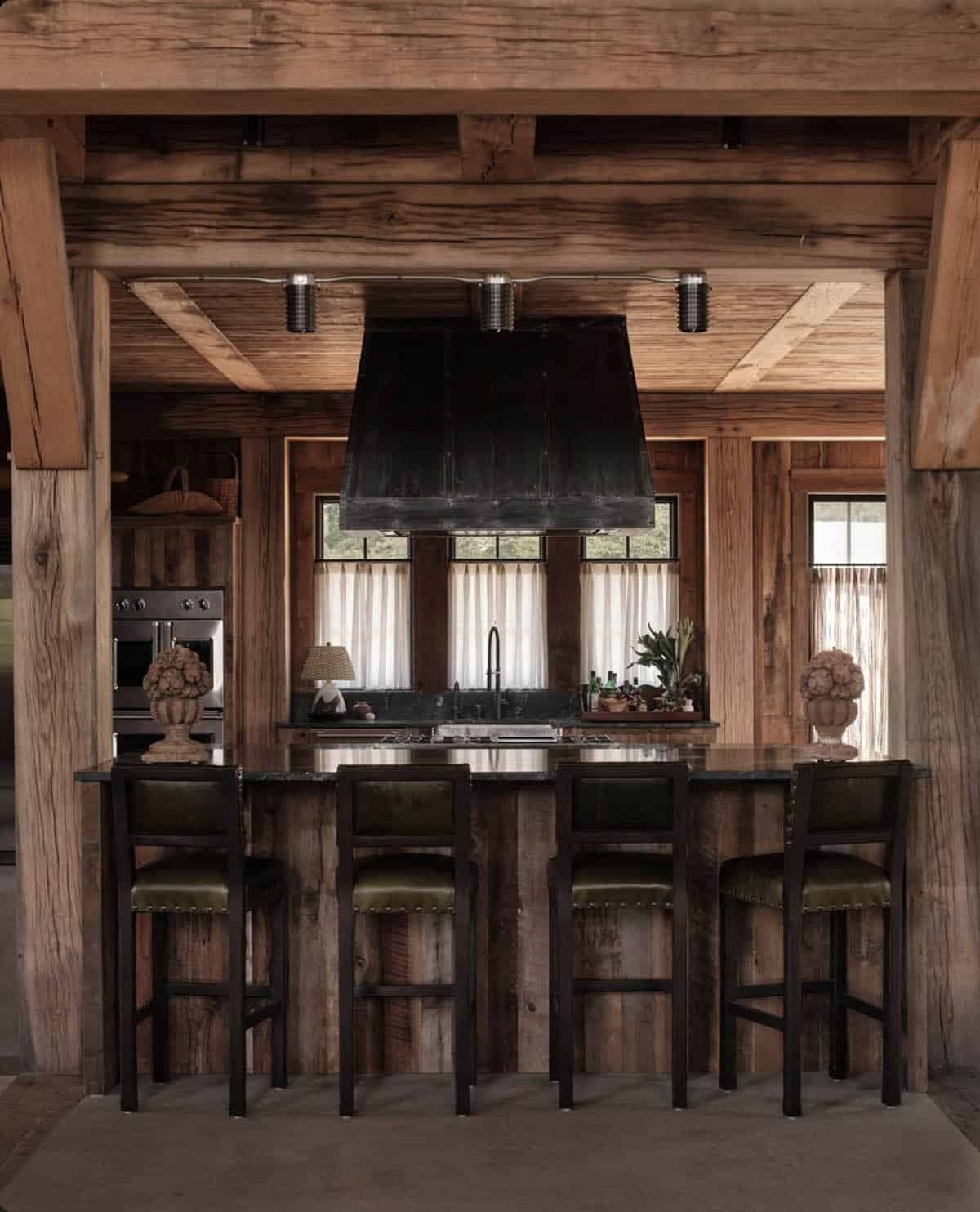 Kitchen island with leather barstools under a blackened metal hood