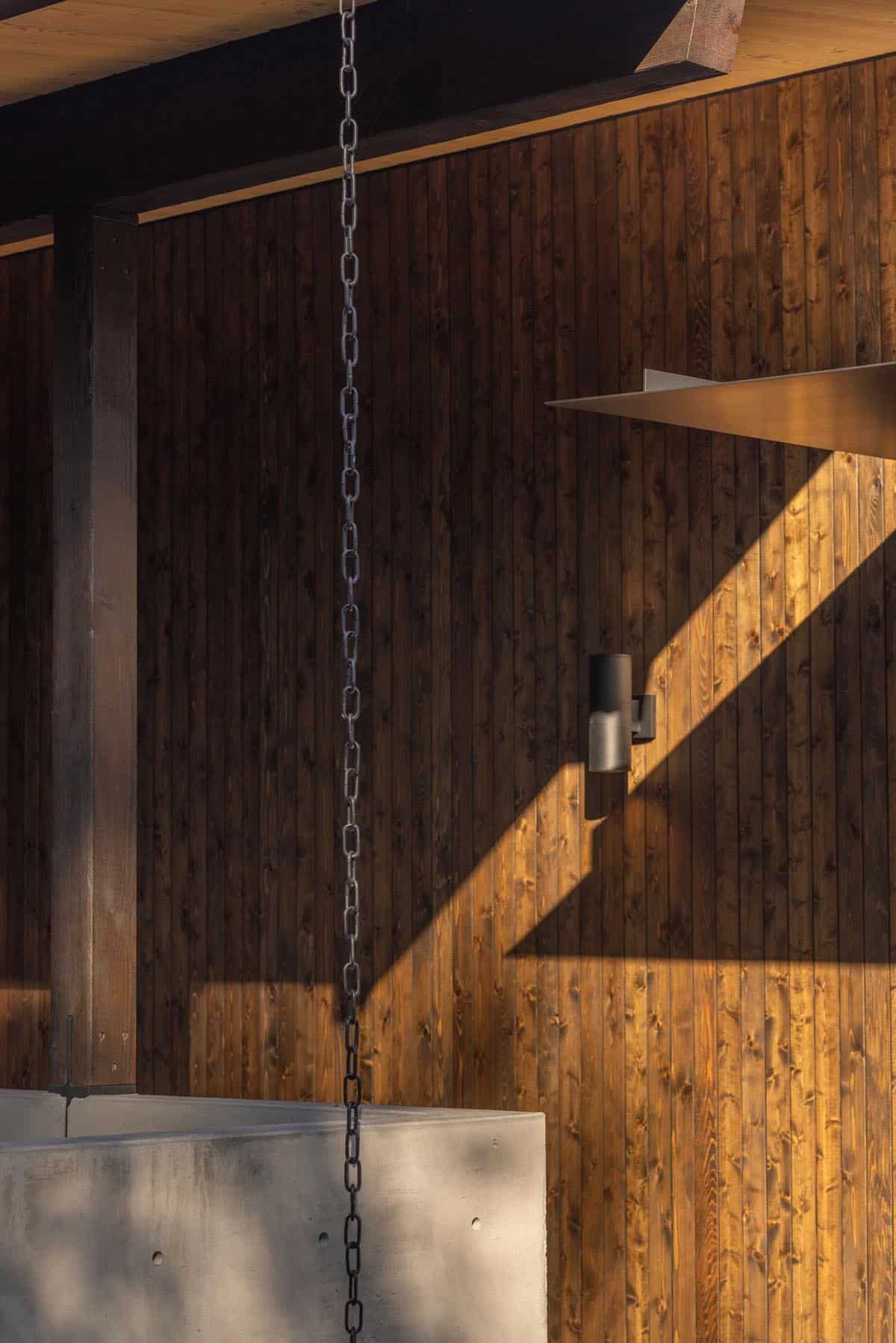 Rain chain hanging past stained cedar wall with black cylinder sconce