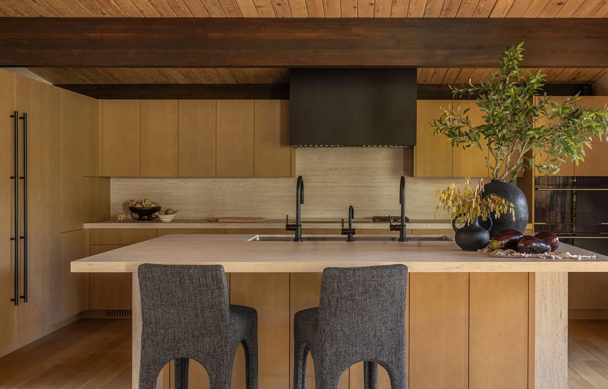 Kitchen with stone-look island, white oak cabinets, dark hood, and upholstered counter stools