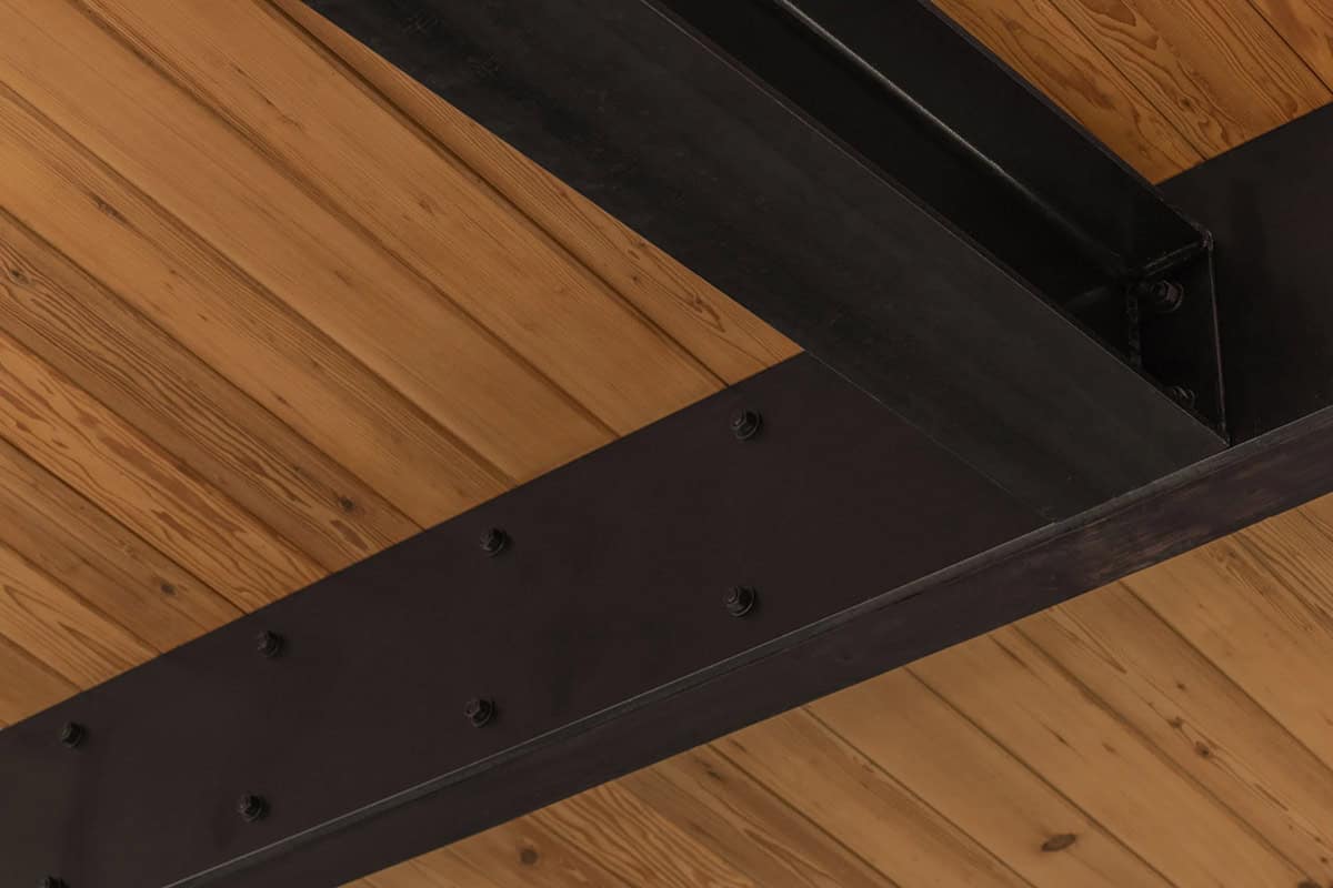 Steel flitch plates bolted to ceiling beams against tongue-and-groove wood ceiling