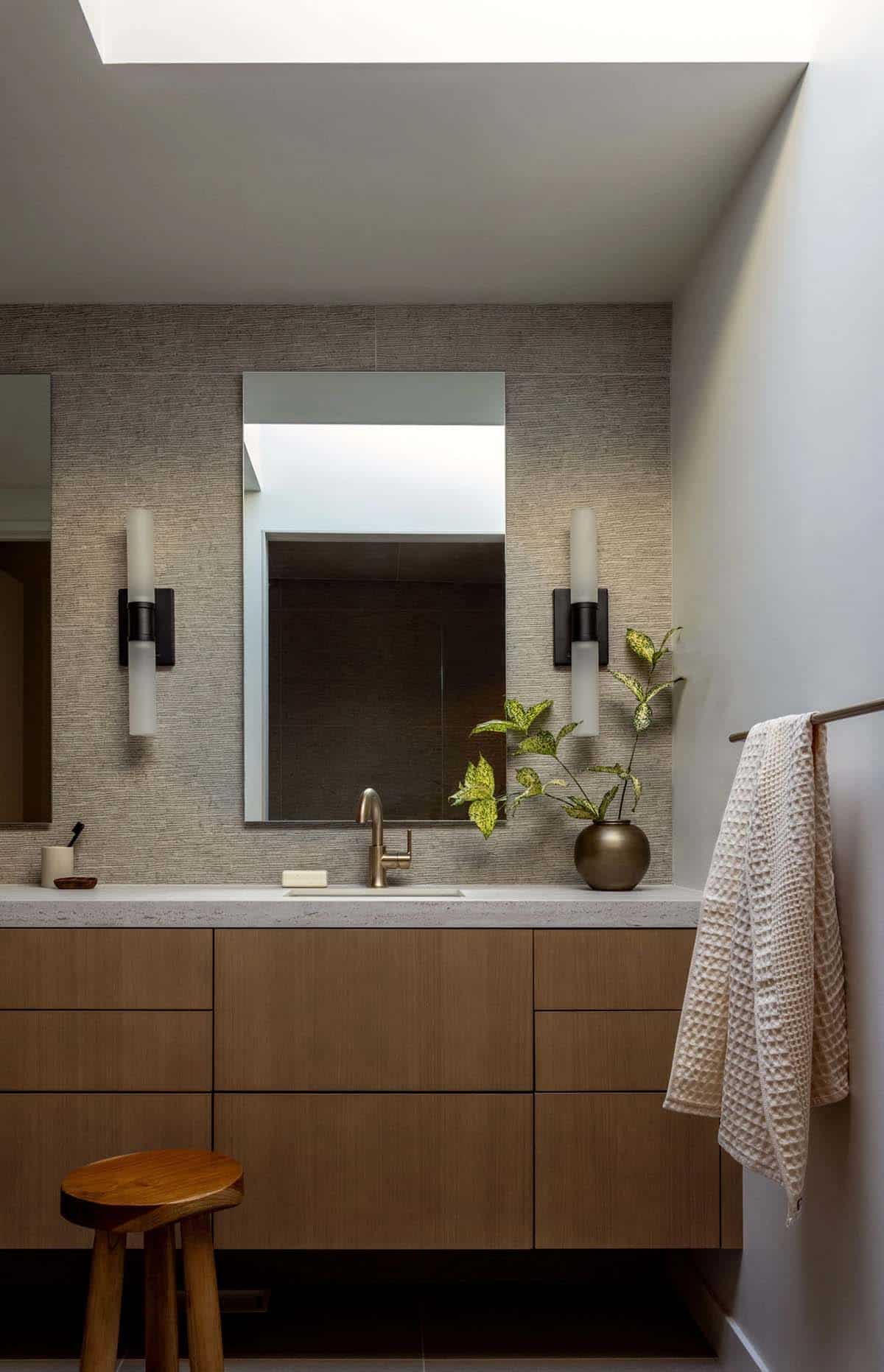 Floating oak vanity with stone-look top, skylight, and frosted glass sconces