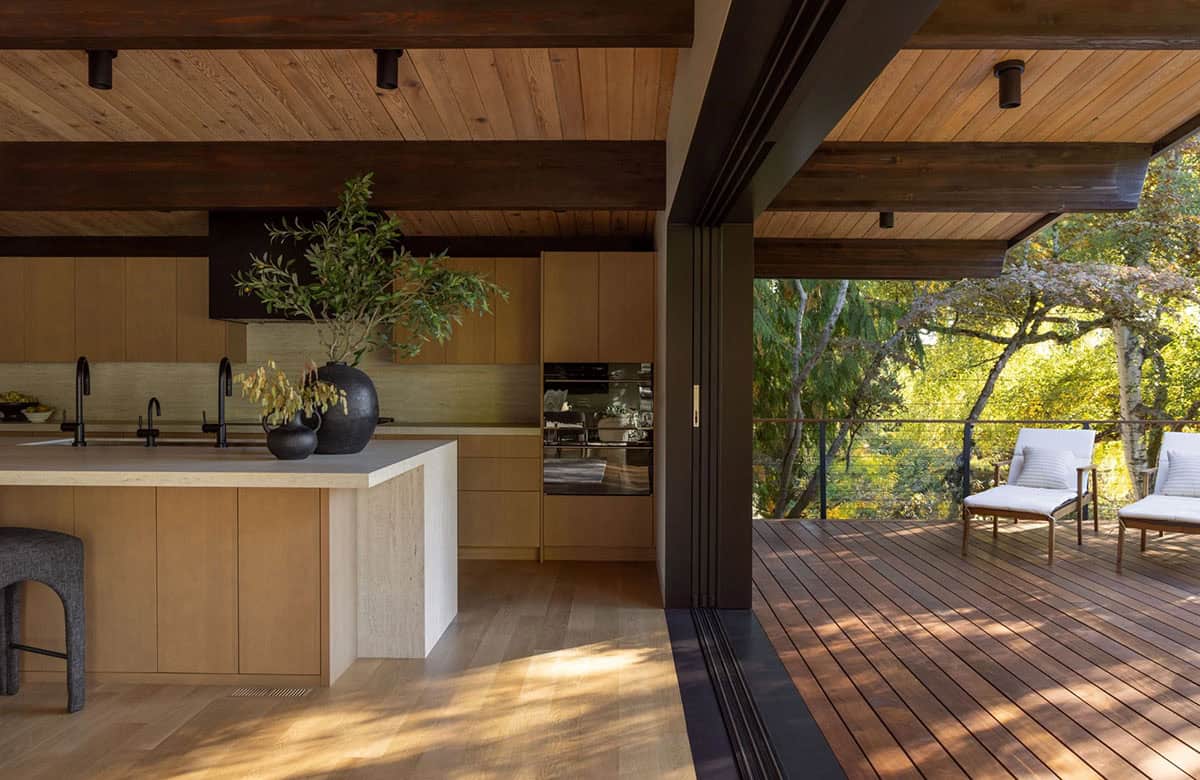 Kitchen opening through sliding glass wall to wood deck with lounge chairs