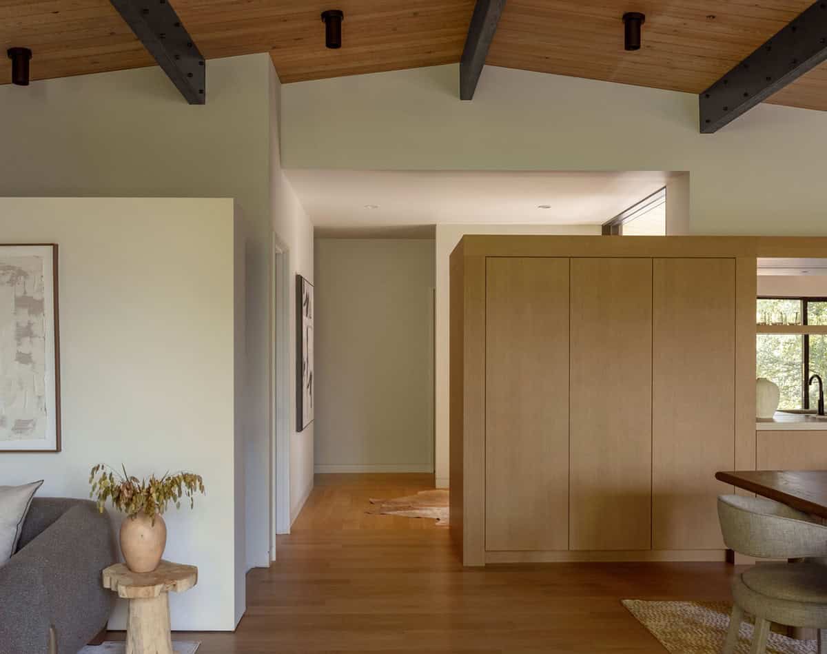 Hallway between white walls and oak storage cabinetry under wood ceiling