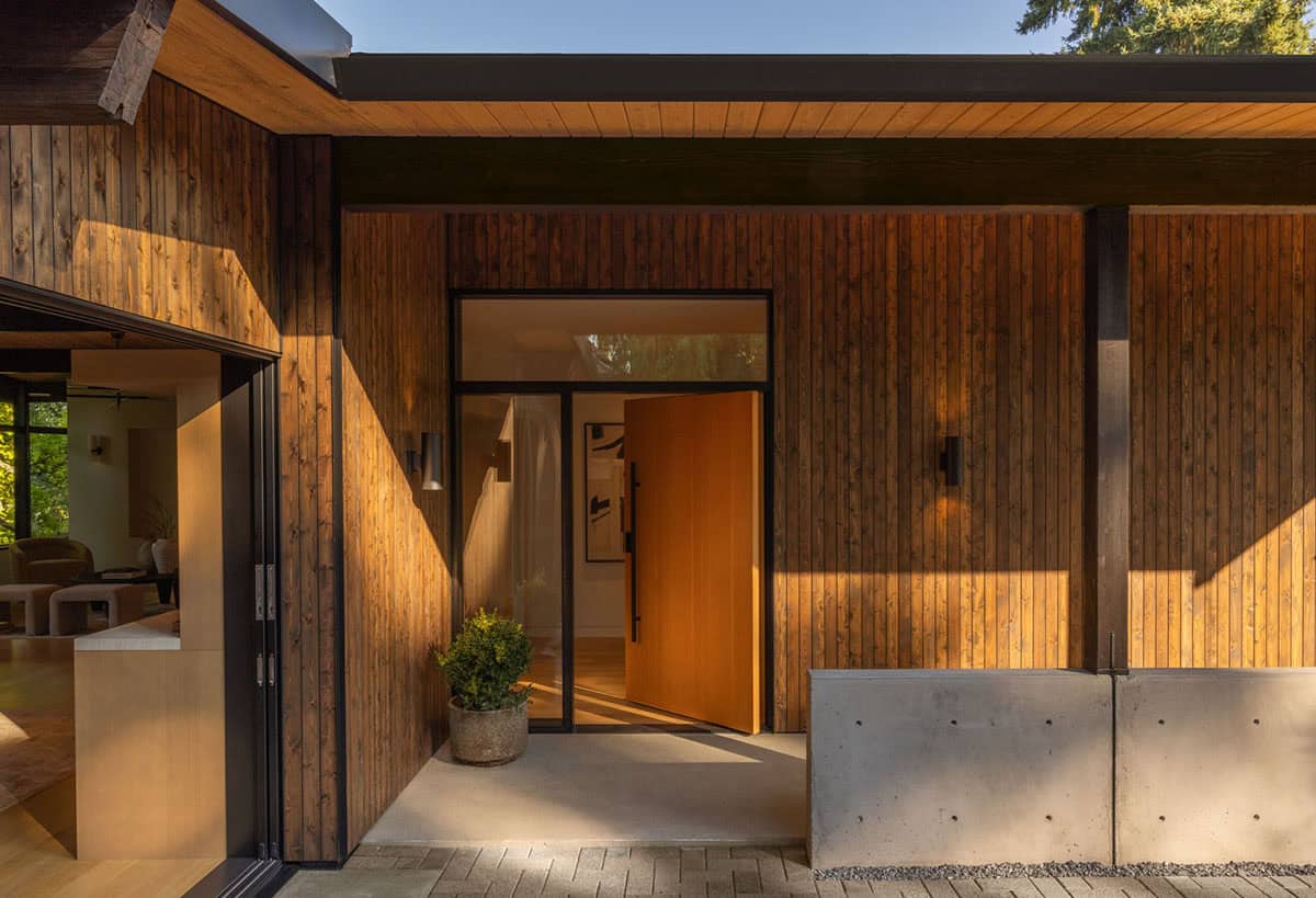 Front entry with glass surround, open oak pivot door, and stained cedar siding