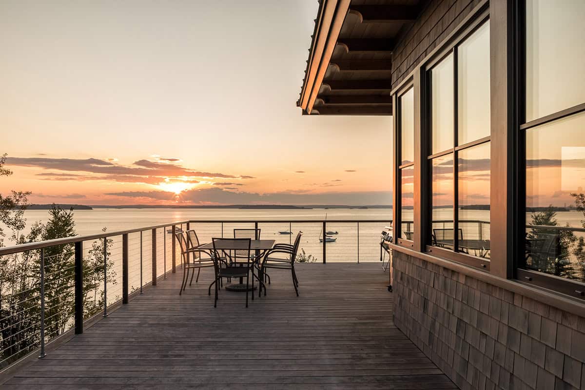 Deck with a dining table and cable railing facing the bay as the sun sets