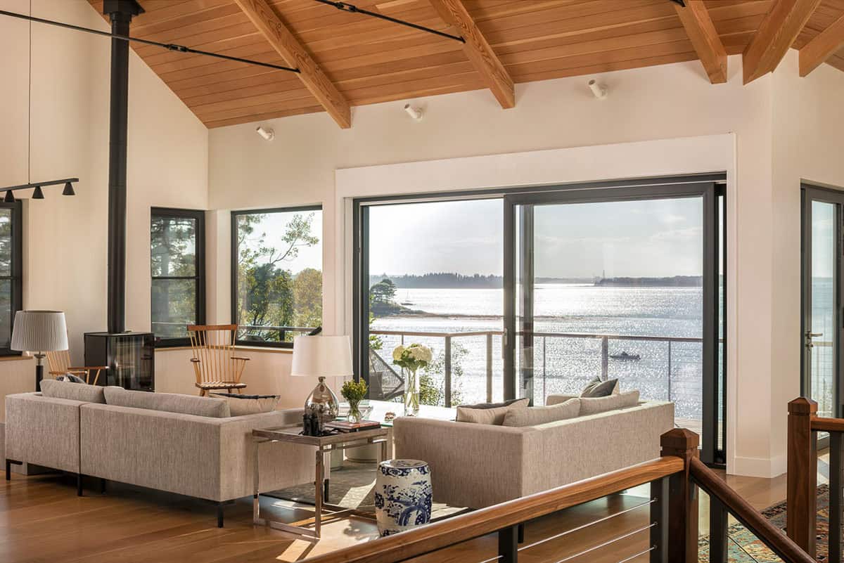 Living room sofas facing a large sliding glass door with sparkling bay views, under a beamed wood ceiling
