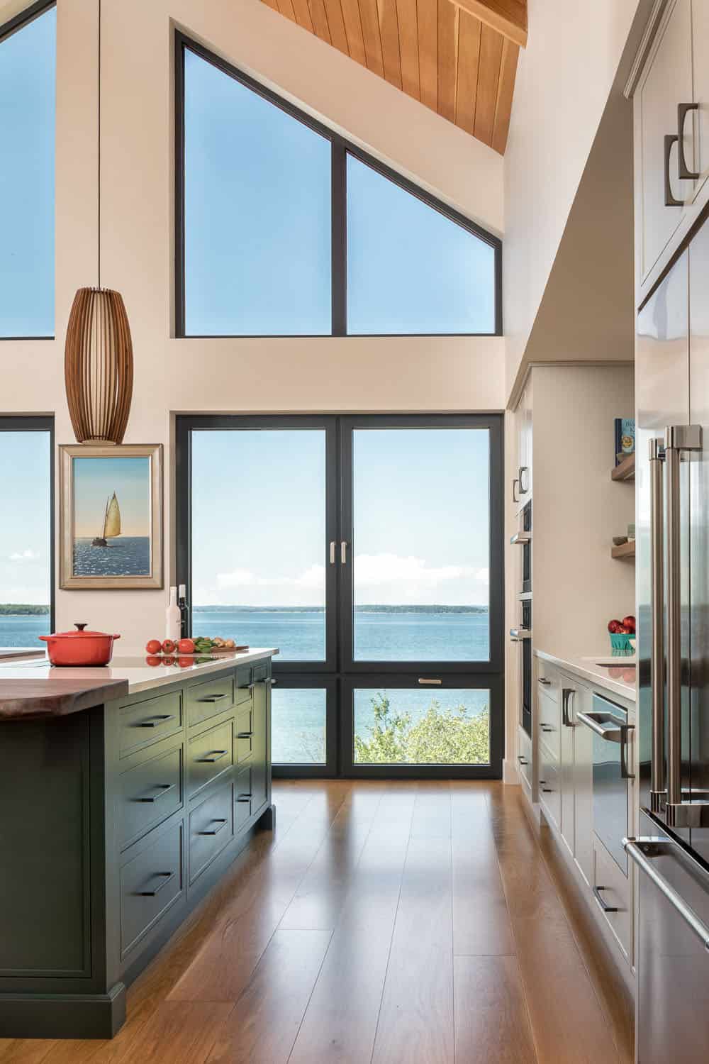 Kitchen with a dark green island and tall windows and doors framing a view of the bay