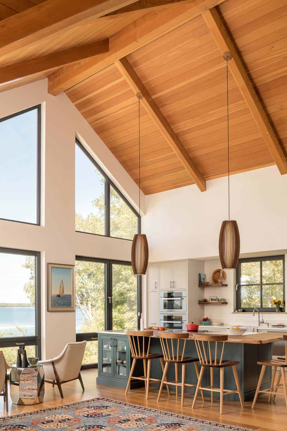 Open kitchen with a dark green island, wood bar stools, and two wood pendant lights under a high beamed ceiling