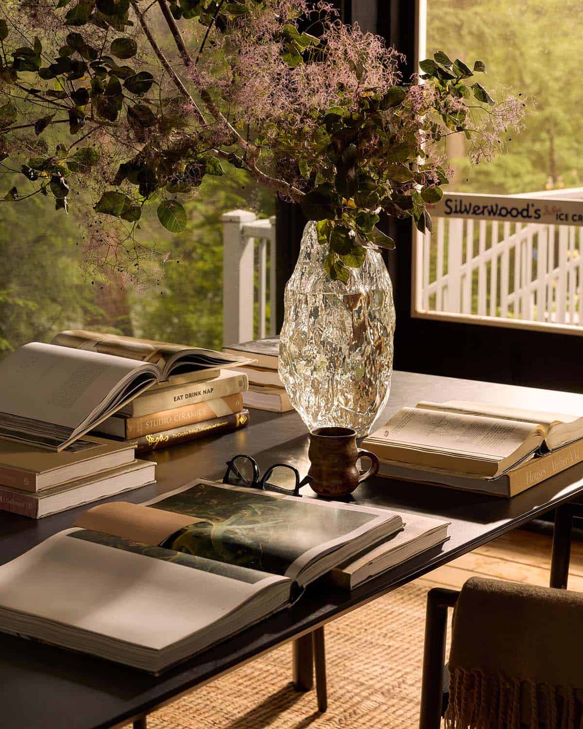 Dining table with stacked books and smoke bush in a glass vase