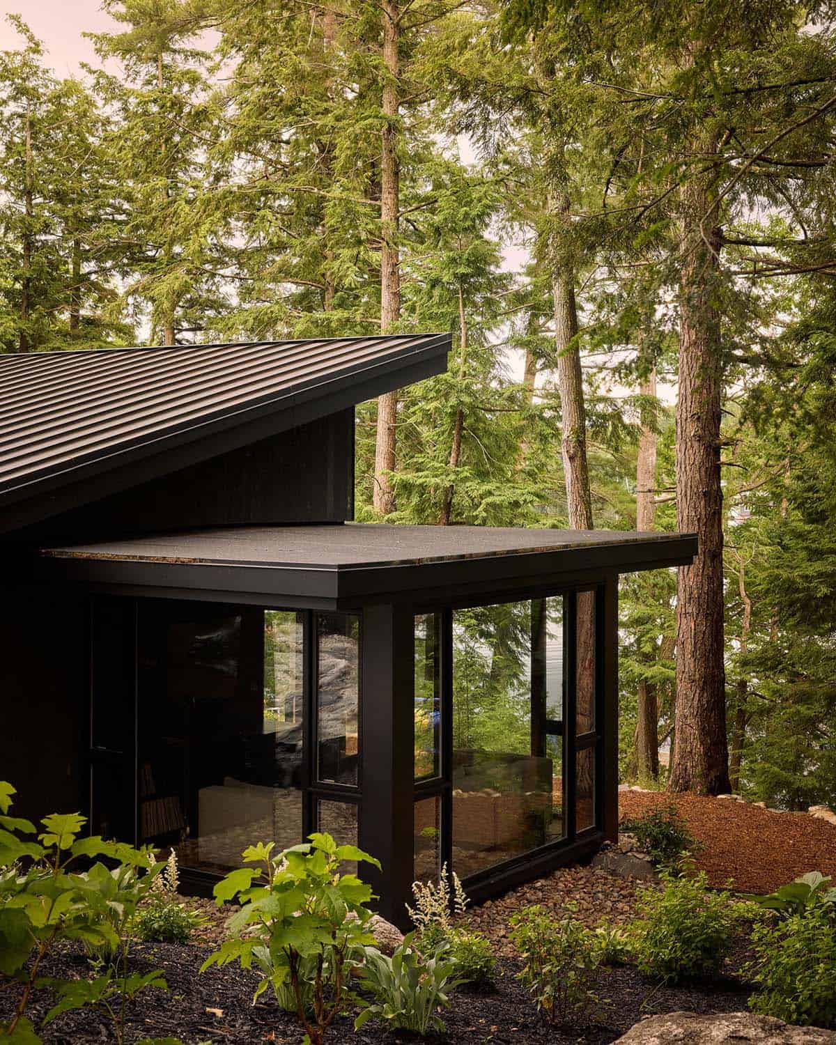 Glass-walled lounge addition among tall pines with lake beyond