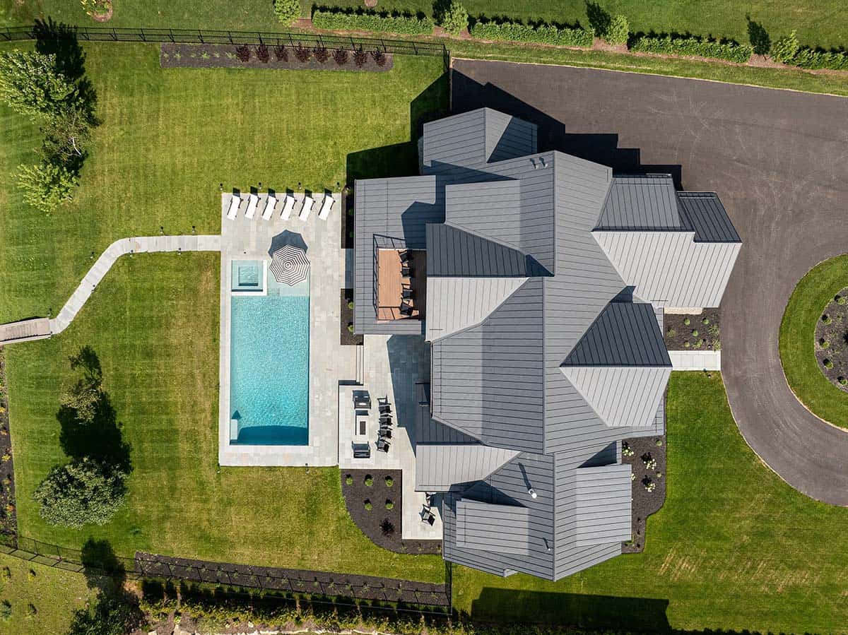 Aerial view of a Vermont modern farmhouse with standing seam metal roofs, pool, and circular asphalt drive