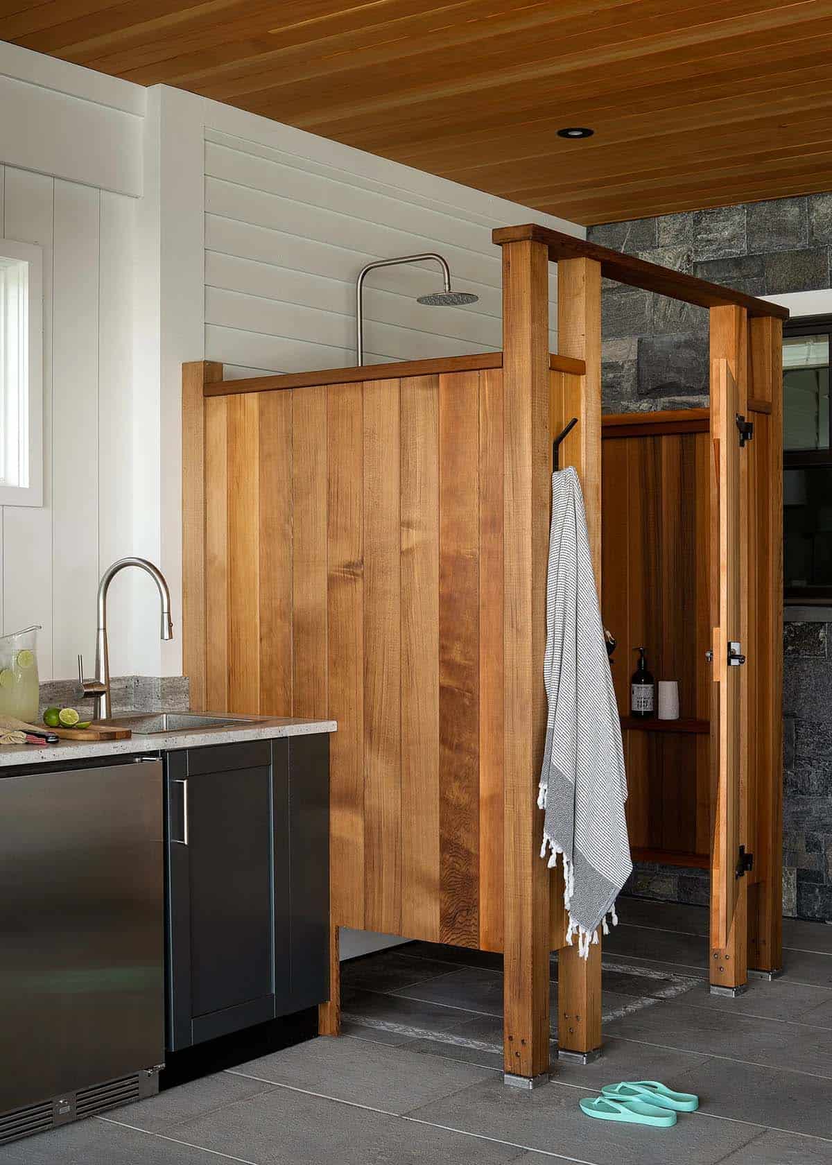 Covered outdoor shower with cedar enclosure beside an outdoor kitchen sink, with a stone wall and cedar ceiling