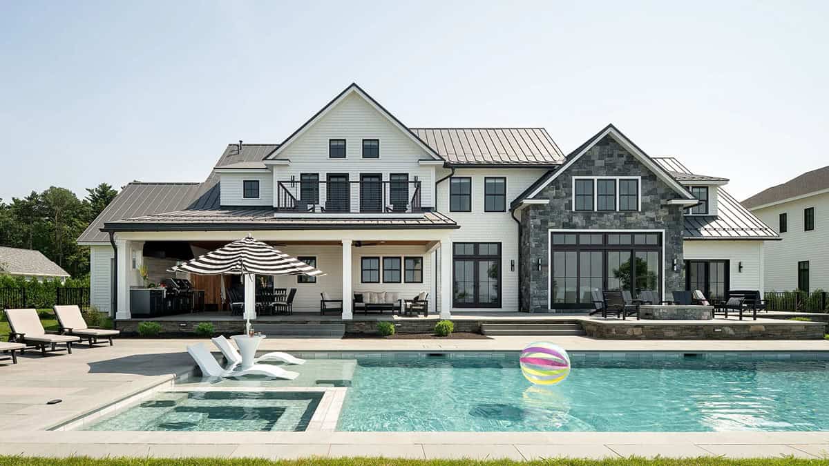 Rear of the modern farmhouse with pool, covered porch, second-floor balcony, and stone-clad gable