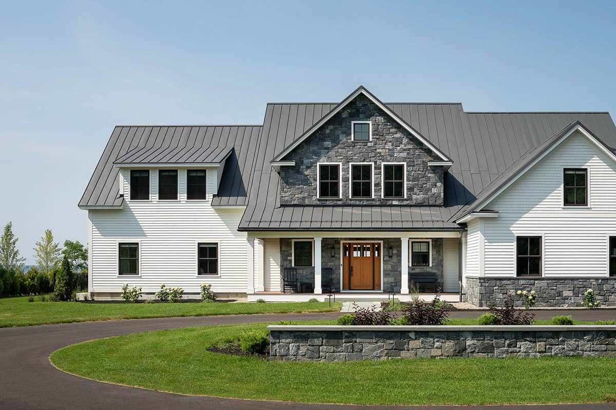 Front of a white clapboard farmhouse with stone gable, standing seam metal roof, wood front door, and stone wall