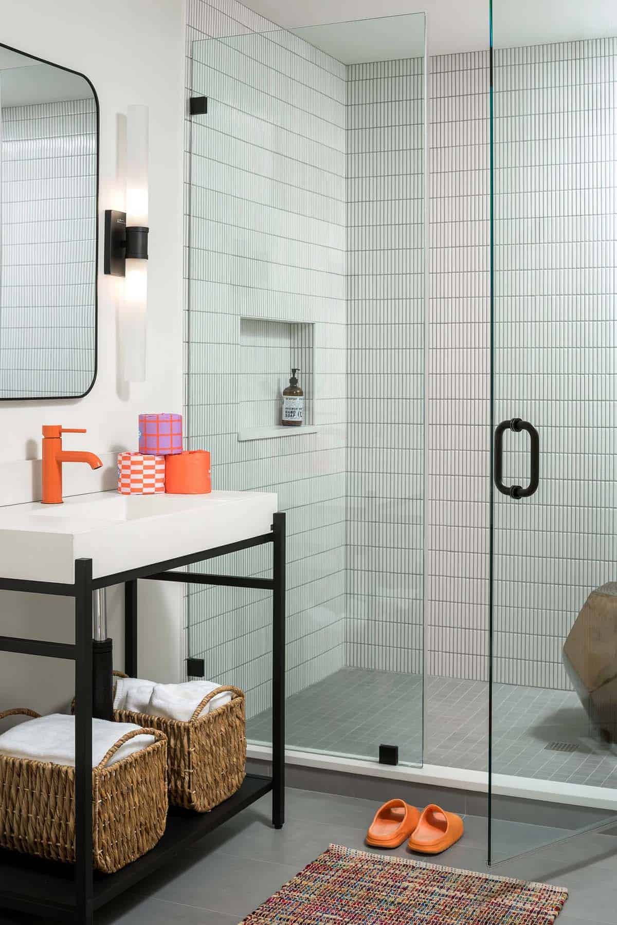 Kids' bathroom with white stacked tile, glass walk-in shower, black metal vanity, and orange faucet