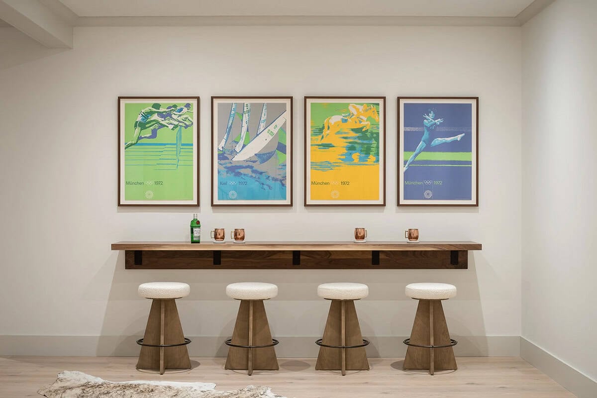 Bar ledge with walnut counter, four wood stools with boucle seats, and vintage Olympic posters