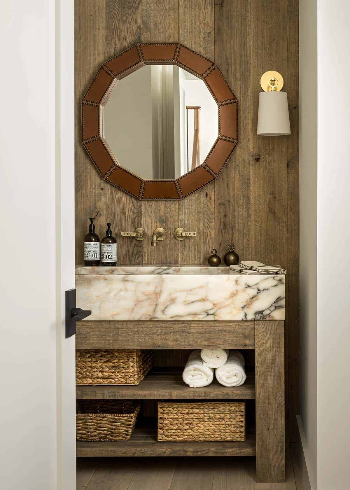 Powder room with marble trough sink on a rustic oak vanity, wall-mounted brass faucet, and leather-framed mirror