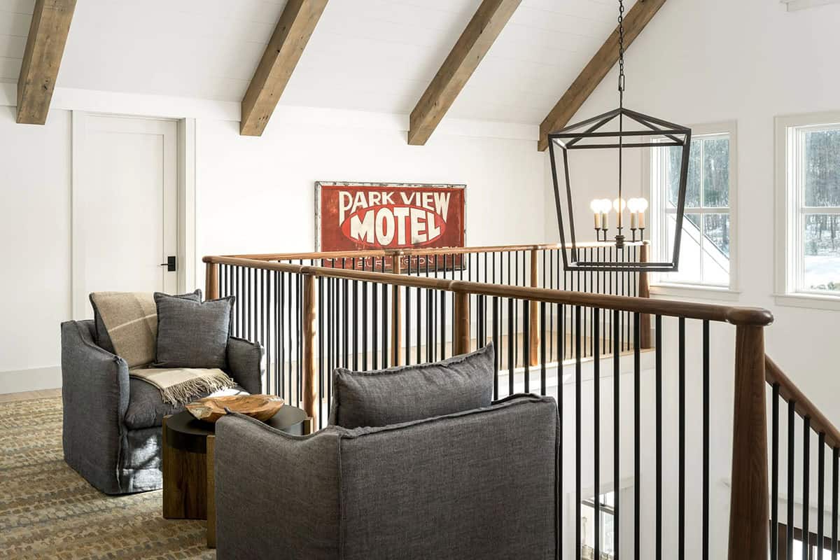 Upstairs landing with vaulted ceiling, wood beams, lantern chandelier, walnut railing, and vintage motel sign