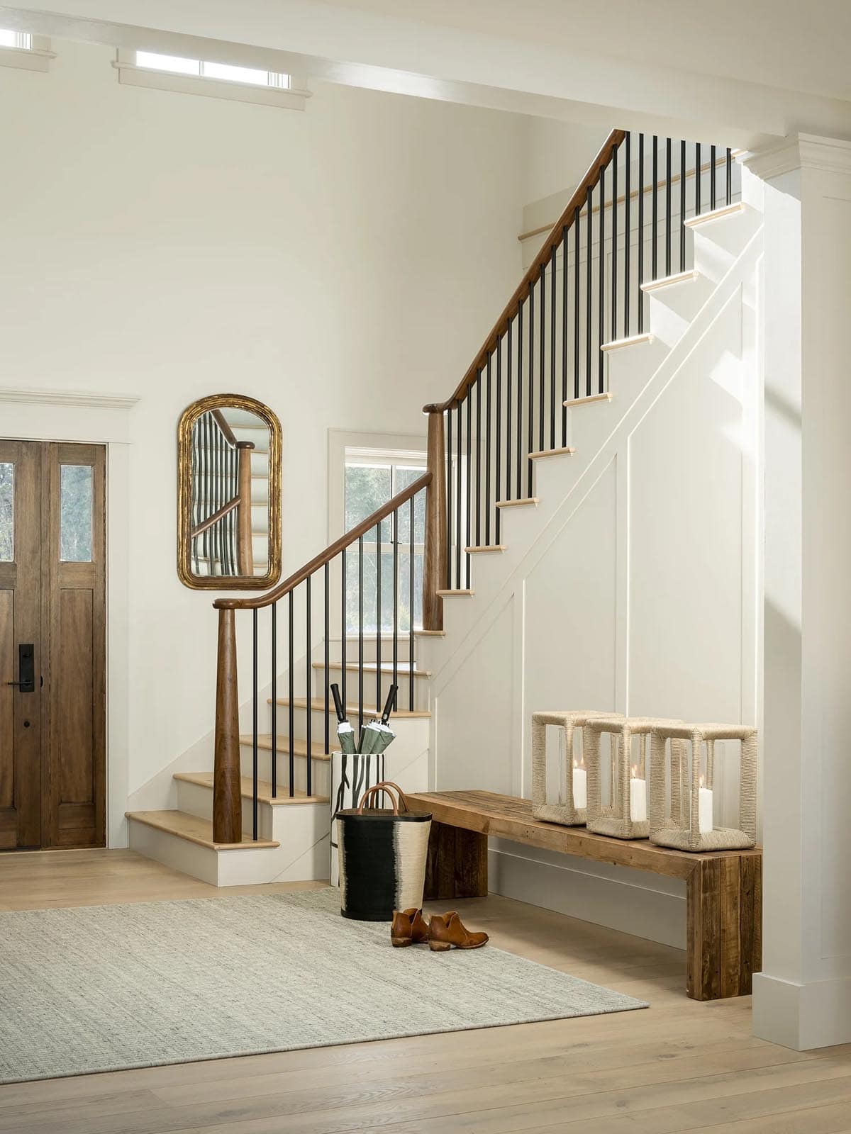 Entry foyer with walnut and black iron staircase, wood front door, gilded mirror, and reclaimed wood bench
