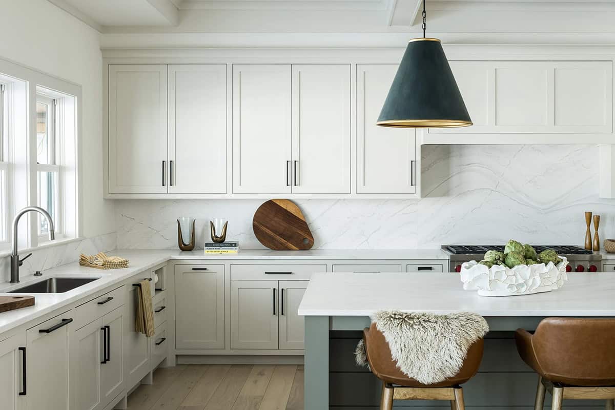 Kitchen with greige Shaker cabinets, marble slab backsplash, black and gold cone pendant, and leather counter stools