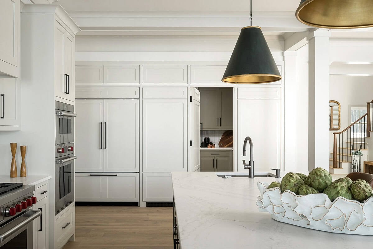 Kitchen with paneled refrigerator, double wall ovens, hidden pantry door, and marble-topped island