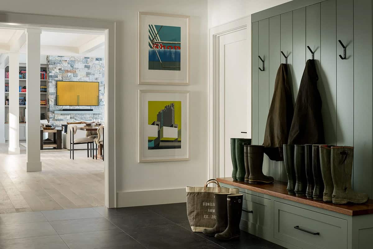 Mudroom with sage green paneled bench, black iron hooks, and dark tile floor, with a view into the living room