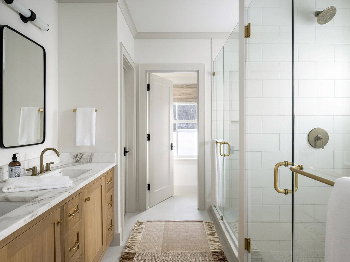 Bathroom with white oak double vanity, marble counter, brass fixtures, and glass-enclosed white tile shower