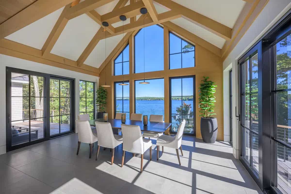 Vaulted dining room with exposed timber beams and floor-to-ceiling windows overlooking the lake