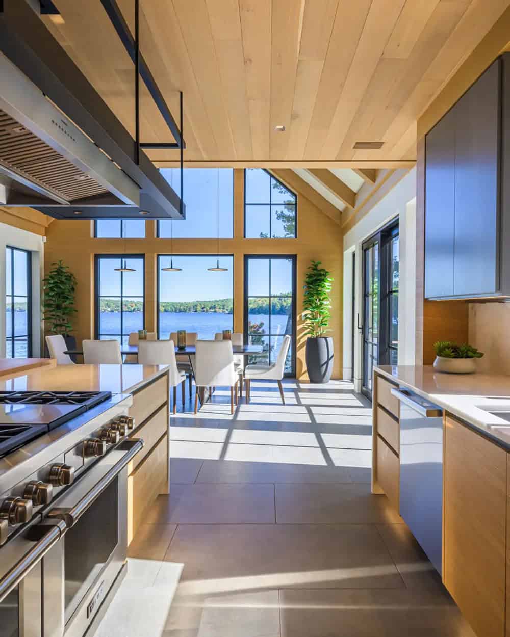 Open kitchen with a hanging range hood, light oak cabinets, and lake views beyond the dining area