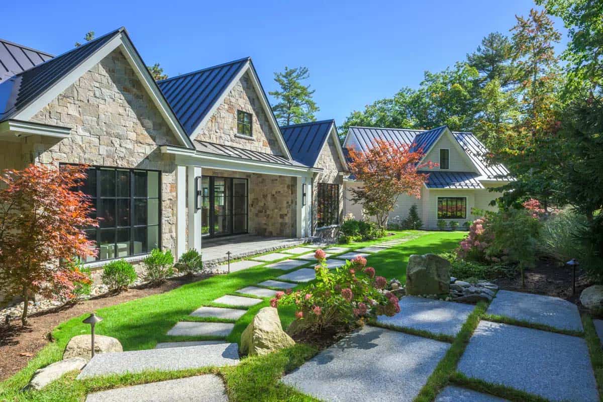 Stone and shingle house entry with a metal roof and a granite stepping-stone path through the lawn