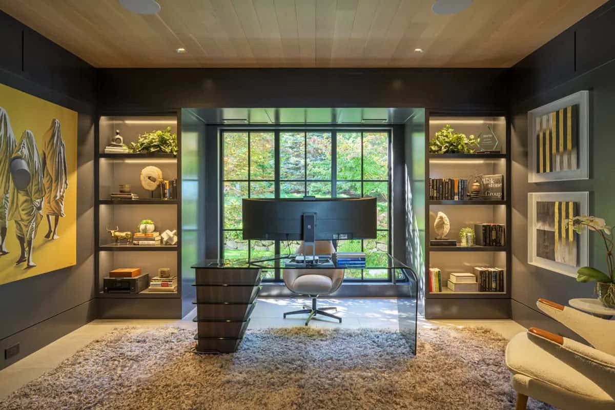 Home office with dark paneled walls, backlit built-in shelves, and a curved glass desk
