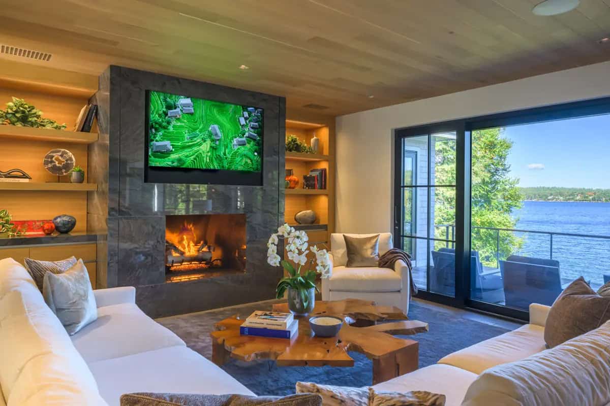 Living room with a stone fireplace, built-in shelves, and a sliding door to the lake-facing deck