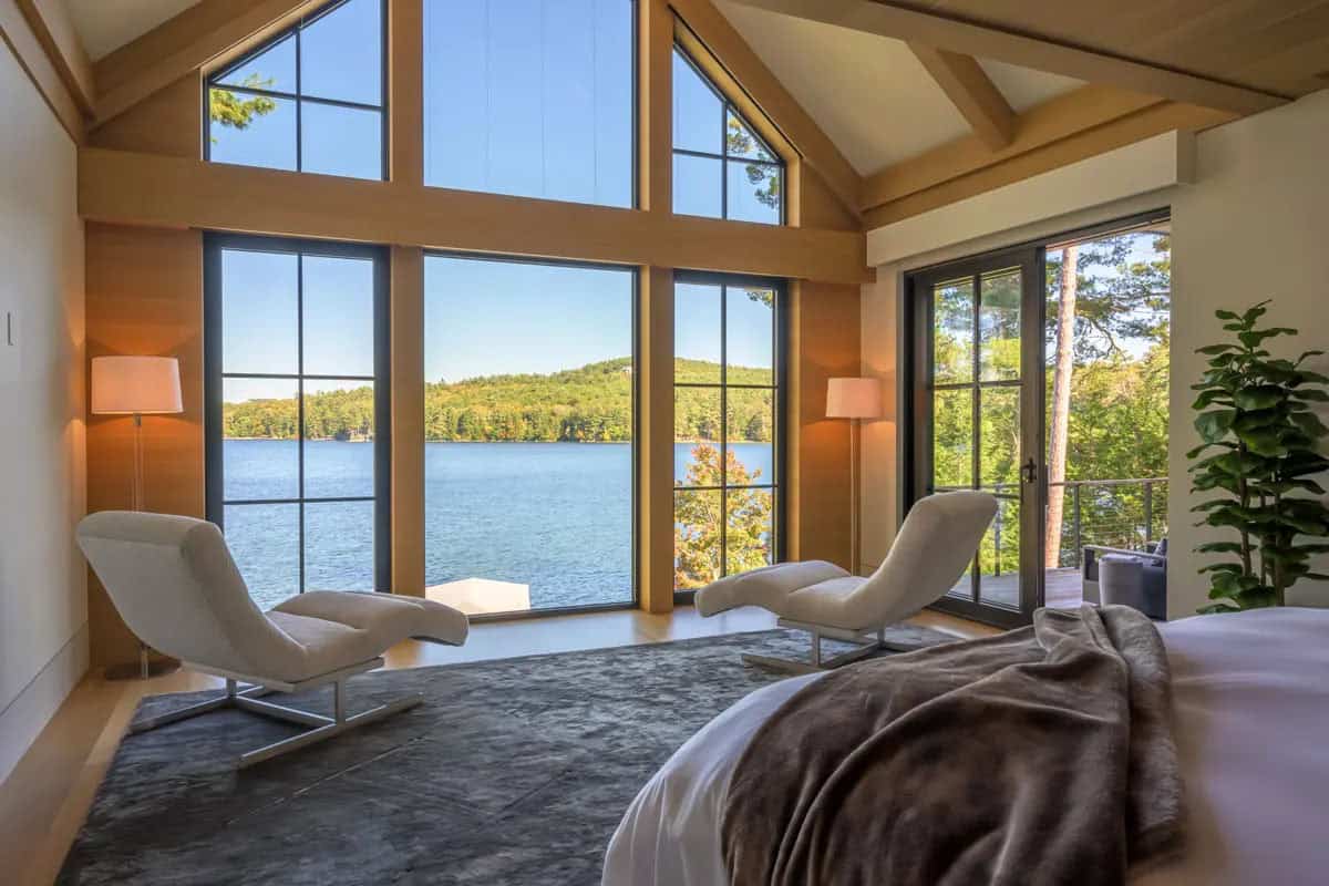 Primary bedroom with a vaulted ceiling, tall lake-view windows, and two white chaise lounges
