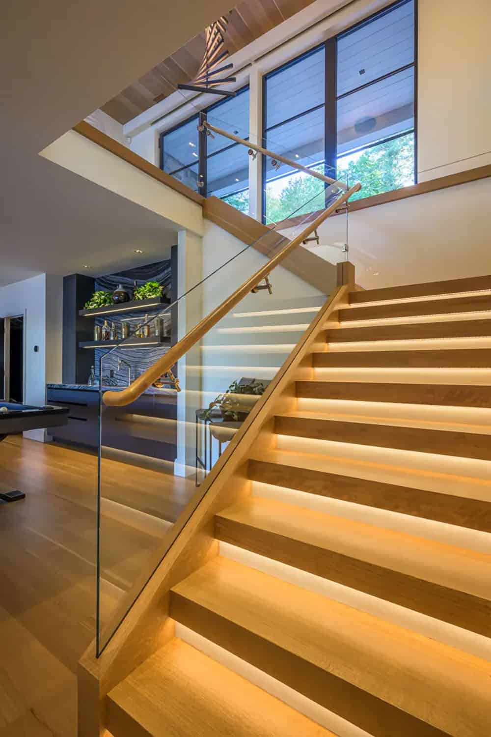 Oak staircase with a glass railing, LED-lit treads, and a wet bar in the background
