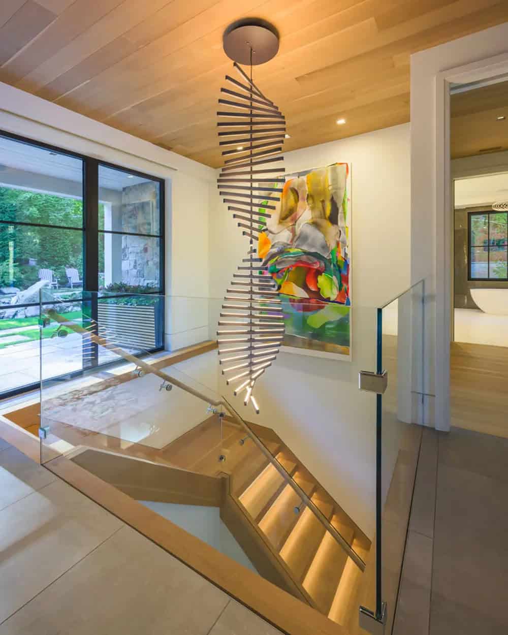 Stairwell with a spiral linear chandelier, glass railings, and a colorful abstract painting