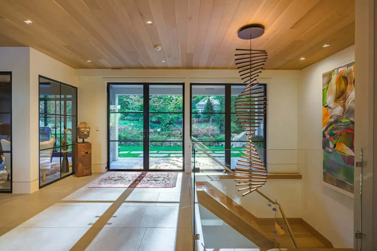 Entry hall with steel-framed glass doors, a sculptural chandelier, and views of the garden