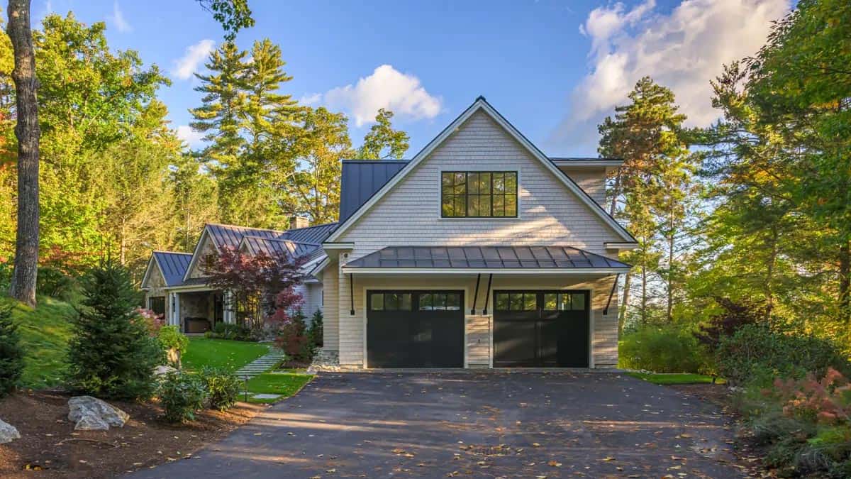 Street-facing garage of a New Hampshire lake house with two black carriage-style doors, a metal awning, and shingled gable above