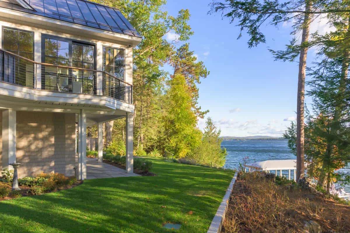 Lakeside corner of the house with a cable-rail balcony, lawn, and boat dock beyond