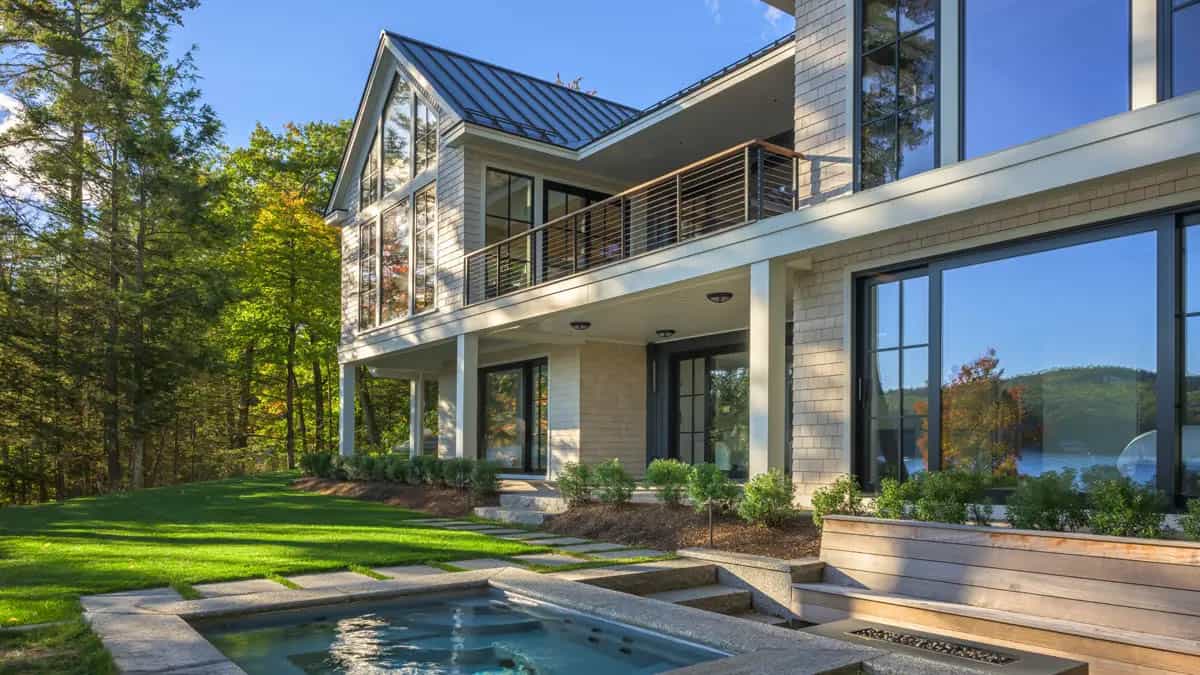 Backyard hot tub with granite surround and a wood fire feature beside the house's glass-walled lakeside facade
