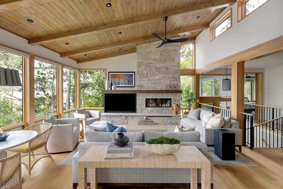 Great room with stone fireplace, timber ceiling, and gray sofas beside lake-facing windows