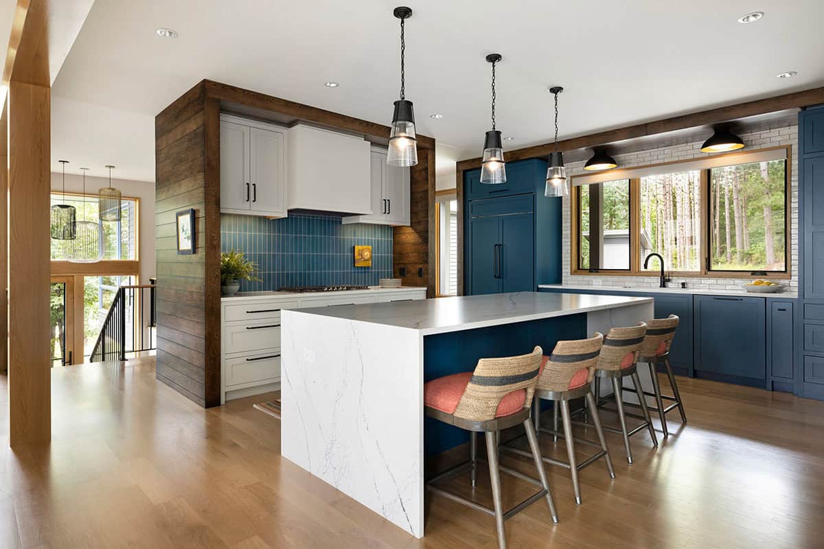 Kitchen with blue cabinetry, waterfall island, woven bar stools, and glass pendant lights