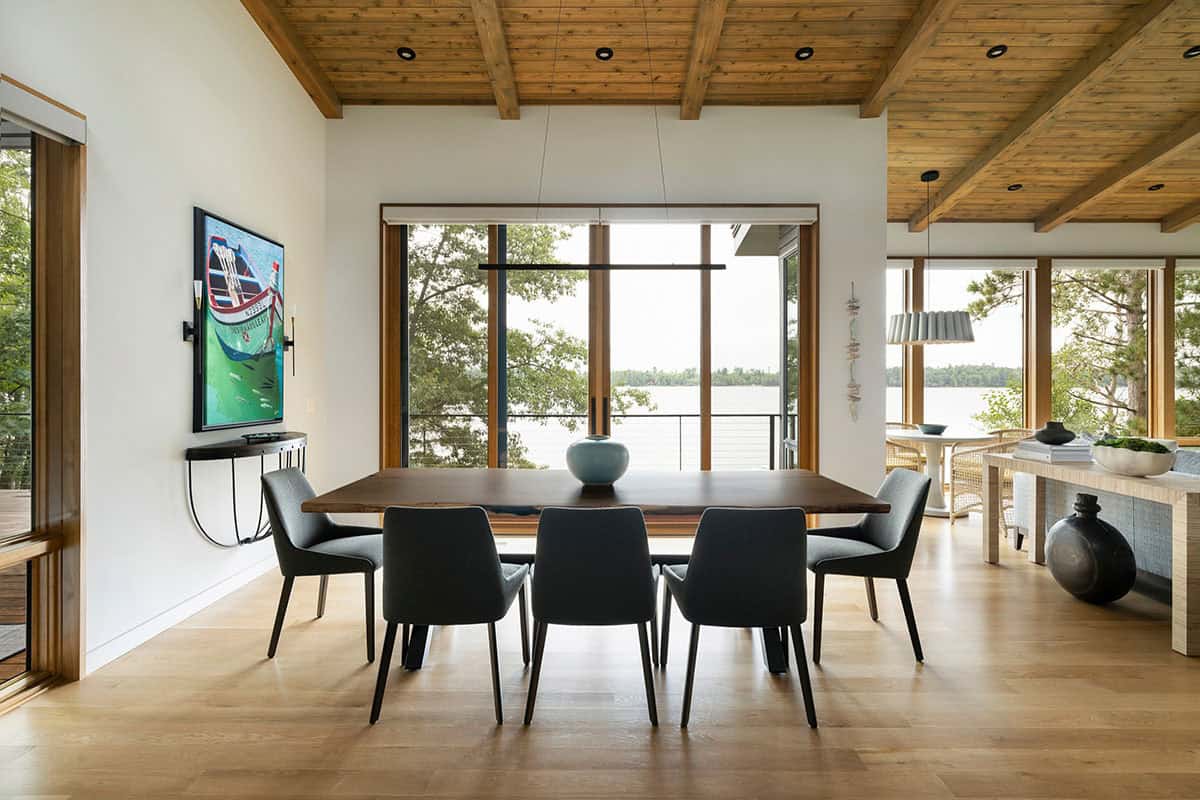 Dining area with live-edge table, gray chairs, and a wall of windows facing the lake