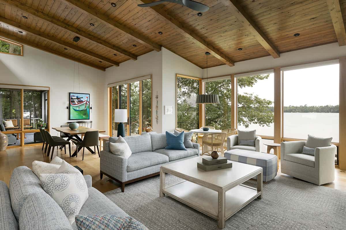 Open living and dining area with lake views, gray sofas, and a vaulted wood ceiling
