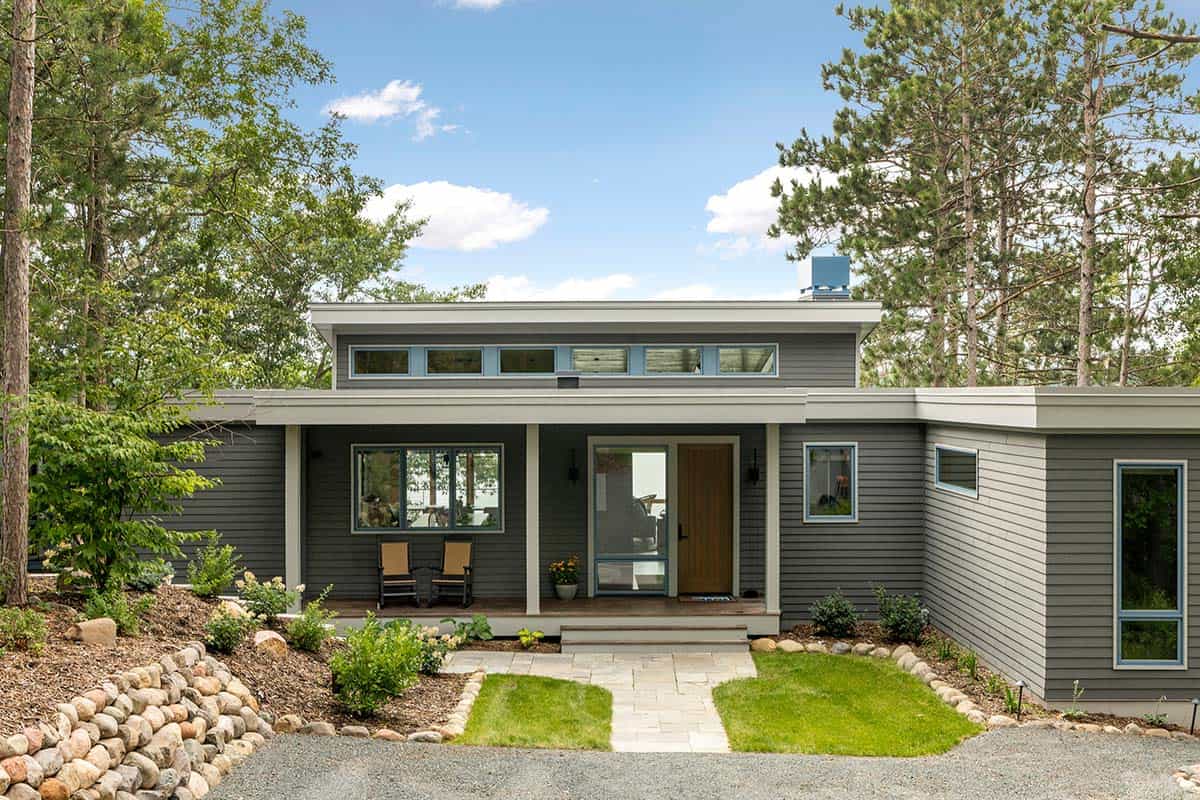 Gray lakeside home entry with a covered porch, wood front door, and stone walkway