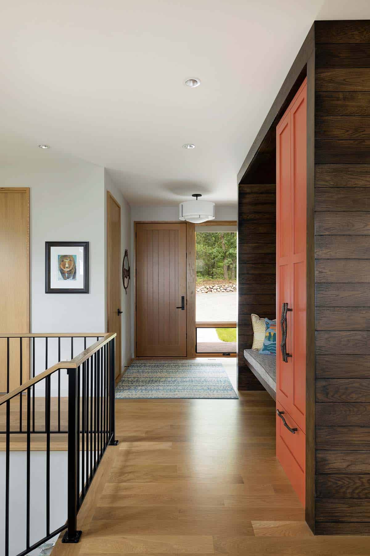 Entry hall with wood front door, black railing, and a coral built-in cabinet beside a bench nook